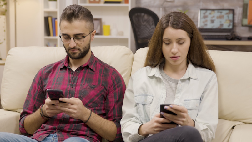 Couple (male, female) sitting on couch with phones in hand experiencing WiFi issues.