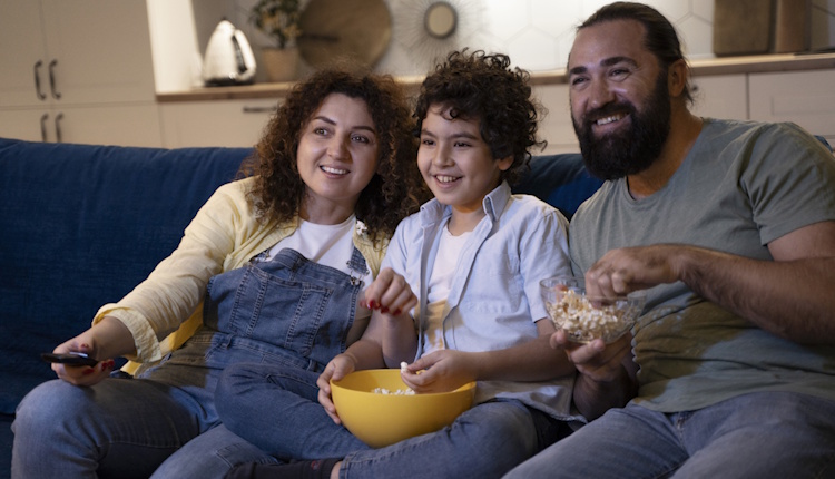 Child sitting with parents, eating popcorn, and watching TV