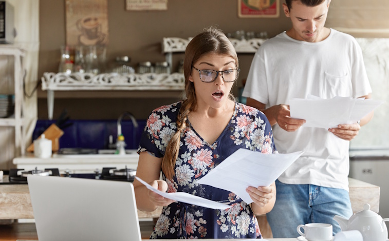 Couple sitting at table in shock at high Internet, TV, and phone bills