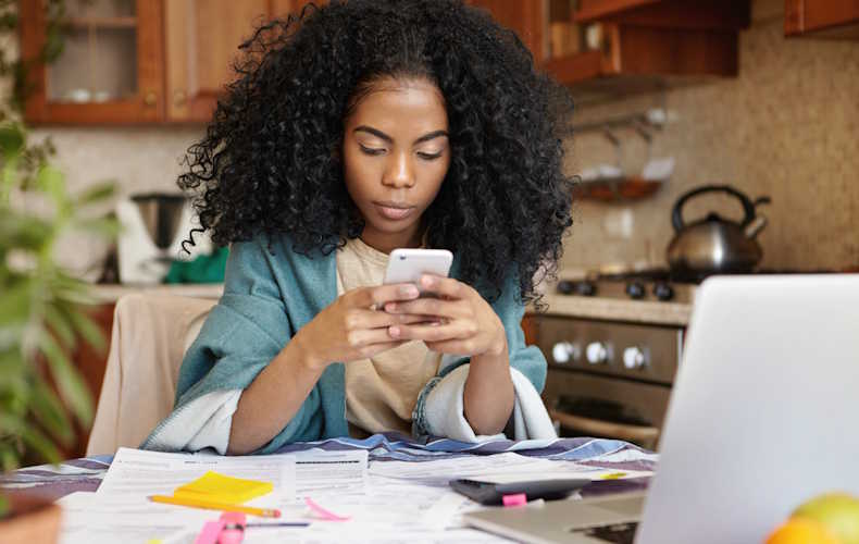 Lady sitting at kitchen table with laptop, Internet and other bills, calculating the total to be paid.