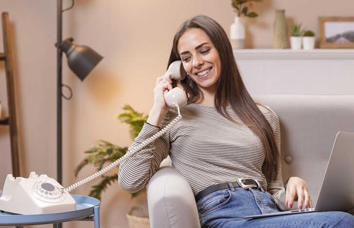 How to switch home phone providers. Lady sitting on couch using laptop + phone powered by NetJOI Digital Phone Service.