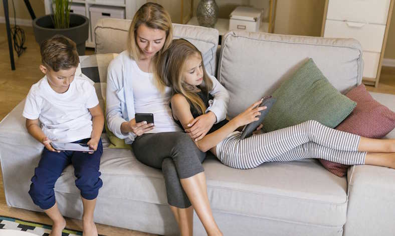 Mom and her two kids sitting together in living room on their devices